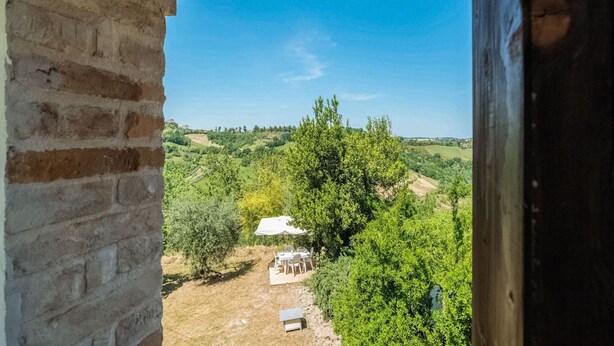 A view from a window overlooking a rural landscape with a small white building and a table with chairs.