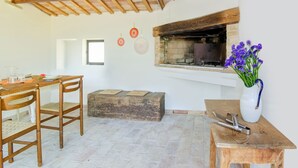 A rustic kitchen with a stone fireplace, wooden beams, and a dining area with chairs and a table. - Holiday home in Torchiaro with garden (Torchiaro)