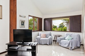 A living room with a flat-screen TV, two grey sofas, a small round table, and a wooden pillar.