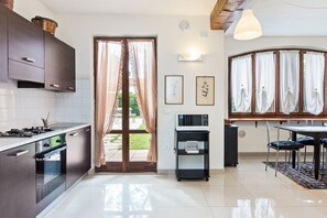 A modern kitchen with stainless steel appliances, a dining area with a table and chairs, and a view through a glass door.