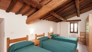 Una habitación con tres camas de madera, techo de madera, un radiador y una ventana.