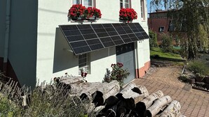 A two-story house with a sloped roof, solar panels, and red flowering plants in the windowsills. - Bright, modern, large vacation apartment on a south-facing slope in a climatic health resort (Friedrichroda)