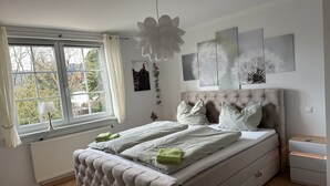 A bedroom with a large bed, a window with curtains, a radiator, and artwork on the wall. - Bright, modern, large vacation apartment on a south-facing slope in a climatic health resort (Friedrichroda)