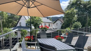 An outdoor patio with a table and chairs, a large umbrella, and potted plants. - Bright, modern, large vacation apartment on a south-facing slope in a climatic health resort (Friedrichroda)