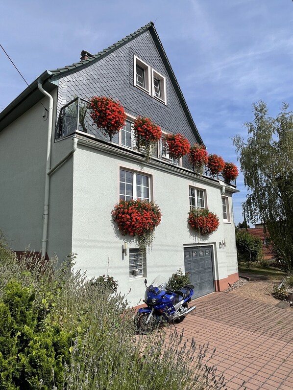 Une maison à deux étages avec un toit gris, des murs blancs et des jardinières rouges sur le balcon.