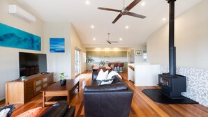 A spacious living room with a fireplace, a dining area, and a kitchen visible through an open door. - Wallace Waves in Mollymook (Mollymook)