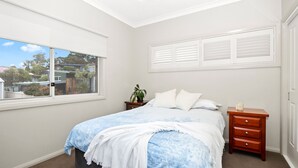 A bedroom with a bed, a nightstand, a dresser, a window, and a view of the outside. - Wallace Waves in Mollymook (Mollymook)