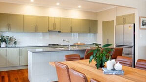 A modern kitchen with light green cabinets, a central island with seating, and a refrigerator. - Wallace Waves in Mollymook (Mollymook)