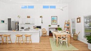 A modern kitchen with white cabinets, a central island with stools, a dining area with a table and chairs, and a ceiling fan. - Break Away in Dolphin Point (Dolphin point)