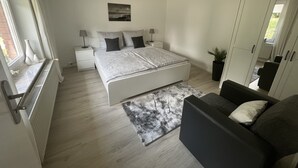 Ein modernes Schlafzimmer mit einem großen Bett, Nachttischen, einer Stehlampe und einem Blick ins Freie.