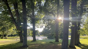 Ein Park mit einem Feldweg, Bäumen und einem Gewässer.