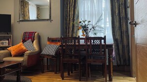 Ein gemütliches Wohnzimmer mit Holzboden, einer Couch, einem Esstisch mit Stühlen und einem großen Fenster mit Vorhängen.