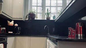 Eine moderne Küche mit grauen Schränken, einer schwarzen Arbeitsplatte, einem roten Wasserkocher und einem Fenster mit Blick auf Gebäude.