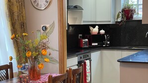 Ein Essbereich mit einem Holztisch und Stühlen, einer Vase mit Blumen und einer durch einen offenen Durchgang einsehbaren Küche.