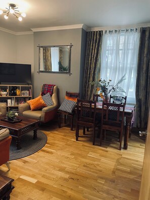 A living room with a television, a sofa, a coffee table, and a dining area with chairs and a table.