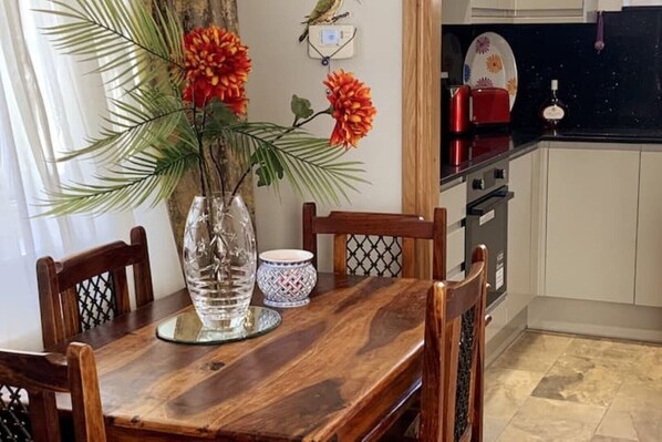 A dining table with a vase of flowers, a decorative bowl, and wooden chairs in a kitchen area with cabinets and a stove.