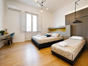 A modern hotel room with two beds, a desk, a chair, and a hanging light fixture.