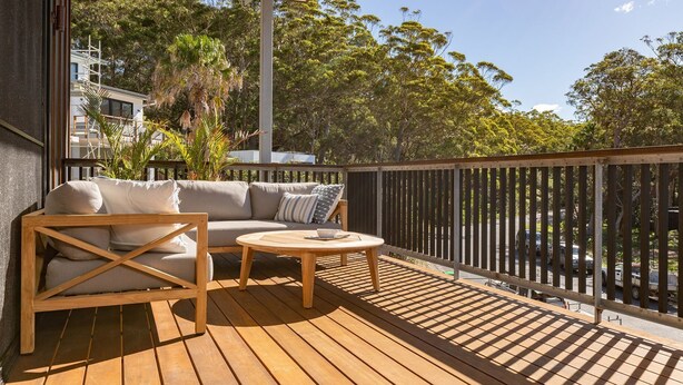 A wooden deck with a sofa and a round table, surrounded by a wooden railing.
