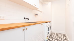 Una cocina con armarios blancos, encimera de madera, pileta y lavadora.