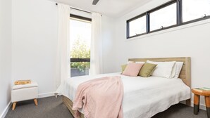 A bedroom with a bed, a nightstand, a window, and a view of greenery outside.