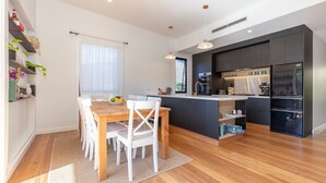 A modern kitchen with dark cabinetry, a wooden dining table, white chairs, and a small island with a sink.