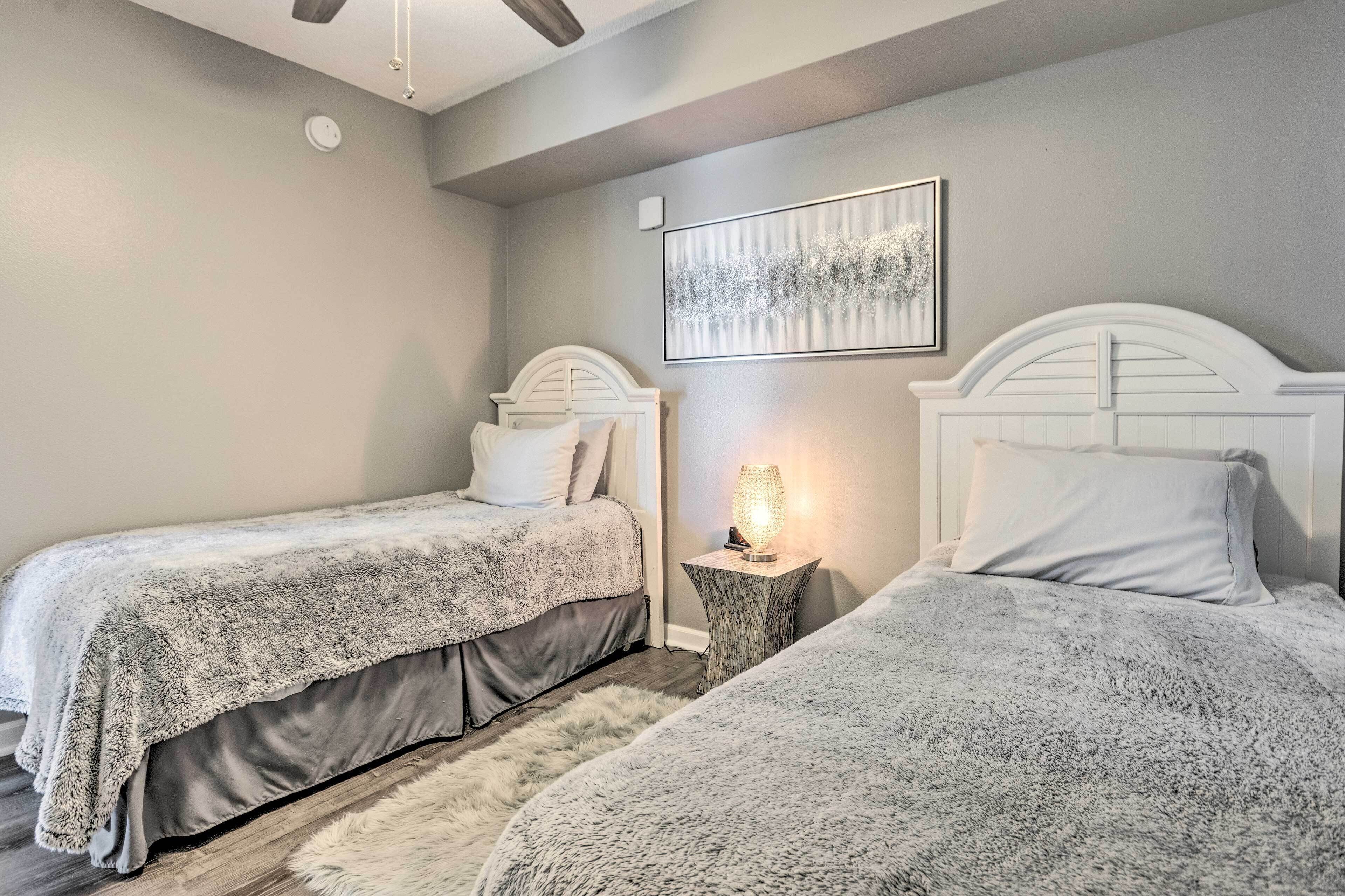 A bedroom with two beds, a nightstand with a lamp, a ceiling fan, and a framed artwork on the wall.