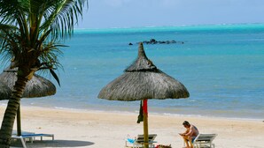 Une plage avec des parasols en chaume, des chaises longues et une personne utilisant un appareil mobile.