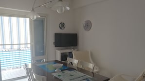 Ein Essbereich mit Tisch, Stühlen, einem Fernseher und einer Wanduhr.
