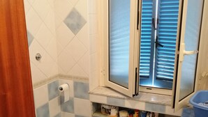 Ein Badezimmer mit Toilette, Dusche und einem Fenster mit Jalousien.
