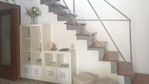 Eine Treppe mit Metallgestell und Holzstufen, die zu einer Zwischenebene mit einem weißen Schrank und Regalen führt.