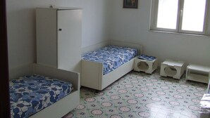 Ein kleines, schlichtes Zimmer mit zwei Betten, einem Kleiderschrank, einem kleinen Tisch und einem Fenster.