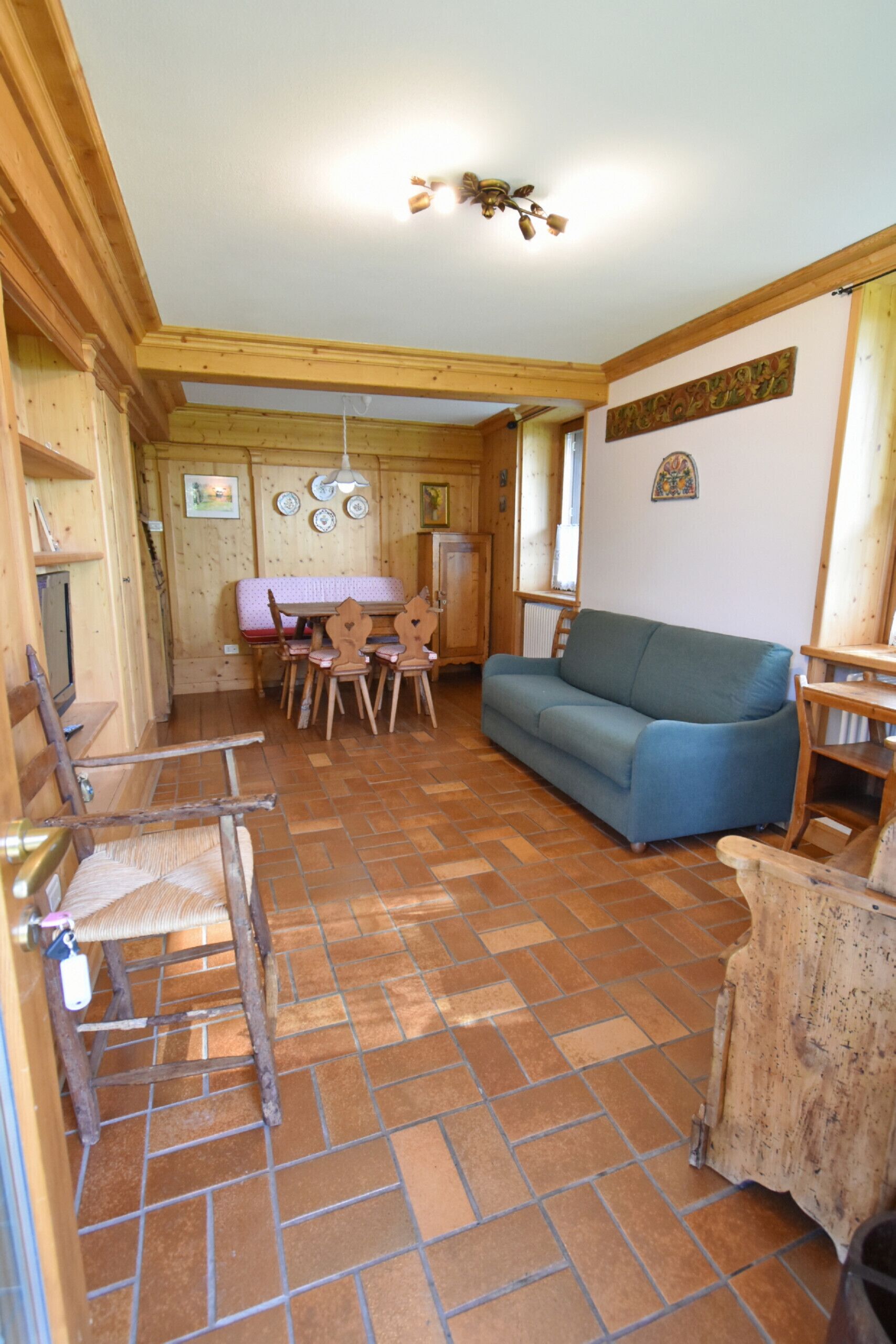 Habitació acollidora amb terra de fusta, un sofà blau, una taula de dinar de fusta amb cadires i un armari de fusta.