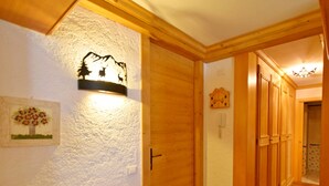 En trægang med bænk, vægmonteret lampe og dør til et andet rum.