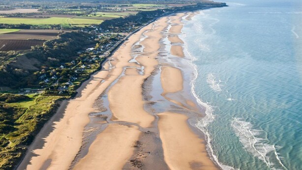 Vista aérea de una zona costera con una extensa playa de arena, campos colindantes y un pequeño poblado.