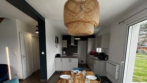 Una cocina moderna con una mesa de comedor de madera dispuesta para seis personas, una lámpara colgante de fibras naturales y vistas al exterior a través de ventanas amplias.