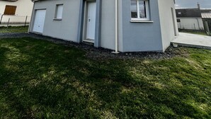 Una casa moderna de dos pisos con techo gris y paredes blancas, una puerta principal y un ventanal pequeño.