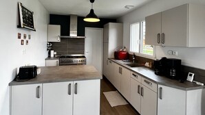Una cocina moderna con armarios blancos, encimera de madera y una lámpara colgante negra.