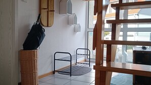 Huoneessa on puinen portaikko, seinälle kiinnitetty hylly, rottinkikori ja metalliteline.