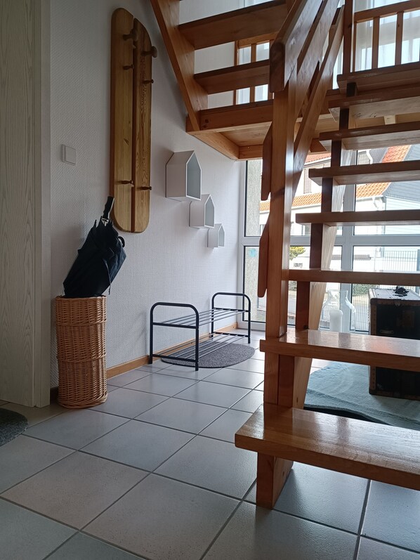 Una habitación con escalera de madera, estante en la pared, cesta de mimbre y un perchero metálico.