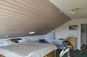 A bedroom with a sloped ceiling, a bed with a quilted cover, a crib, a dresser, and a ceiling fan.