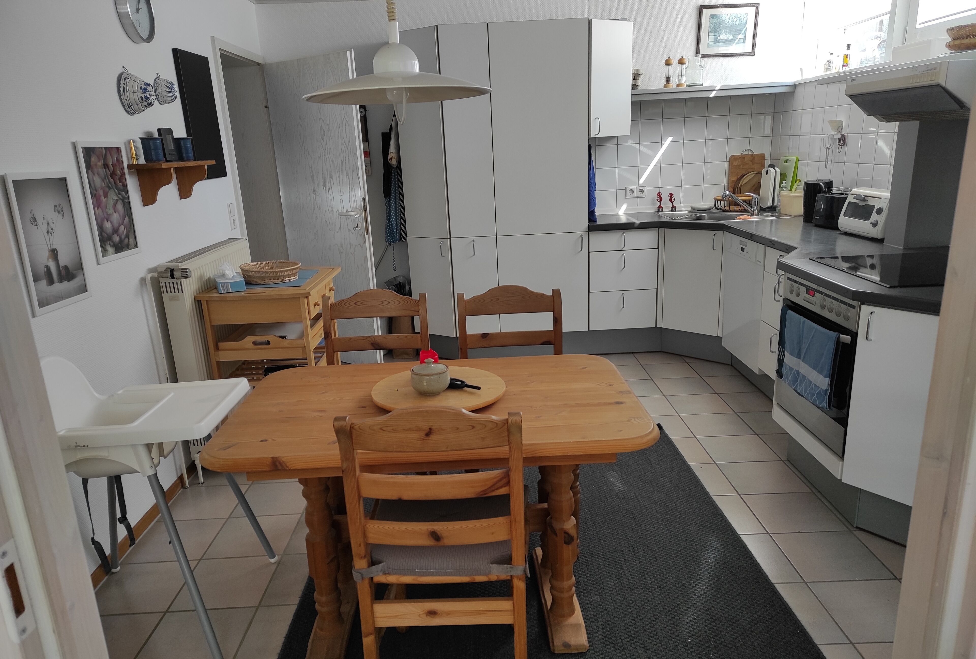 Une cuisine moderne avec des meubles blancs, une table à manger en bois et un tapis noir.