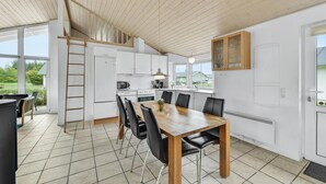 Een moderne keuken met witte kasten, een houten eettafel met zwarte stoelen en uitzicht op het landschap door grote ramen.