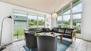Een moderne woonkamer met een zwarte leren bank, een salontafel en een vloerlamp. Grote ramen bieden uitzicht op het groen.