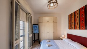 Ein Schlafzimmer mit Bett, Kleiderschrank, einem Gemälde auf Staffelei und einer Tür mit Glasfenstern.