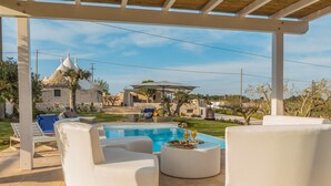 A pool area with white lounge chairs, a round table with food and drinks, and a stone building in the background. - Holiday Home 'Trulli Terralunga' with Pool and Wi-Fi (Martina Franca)