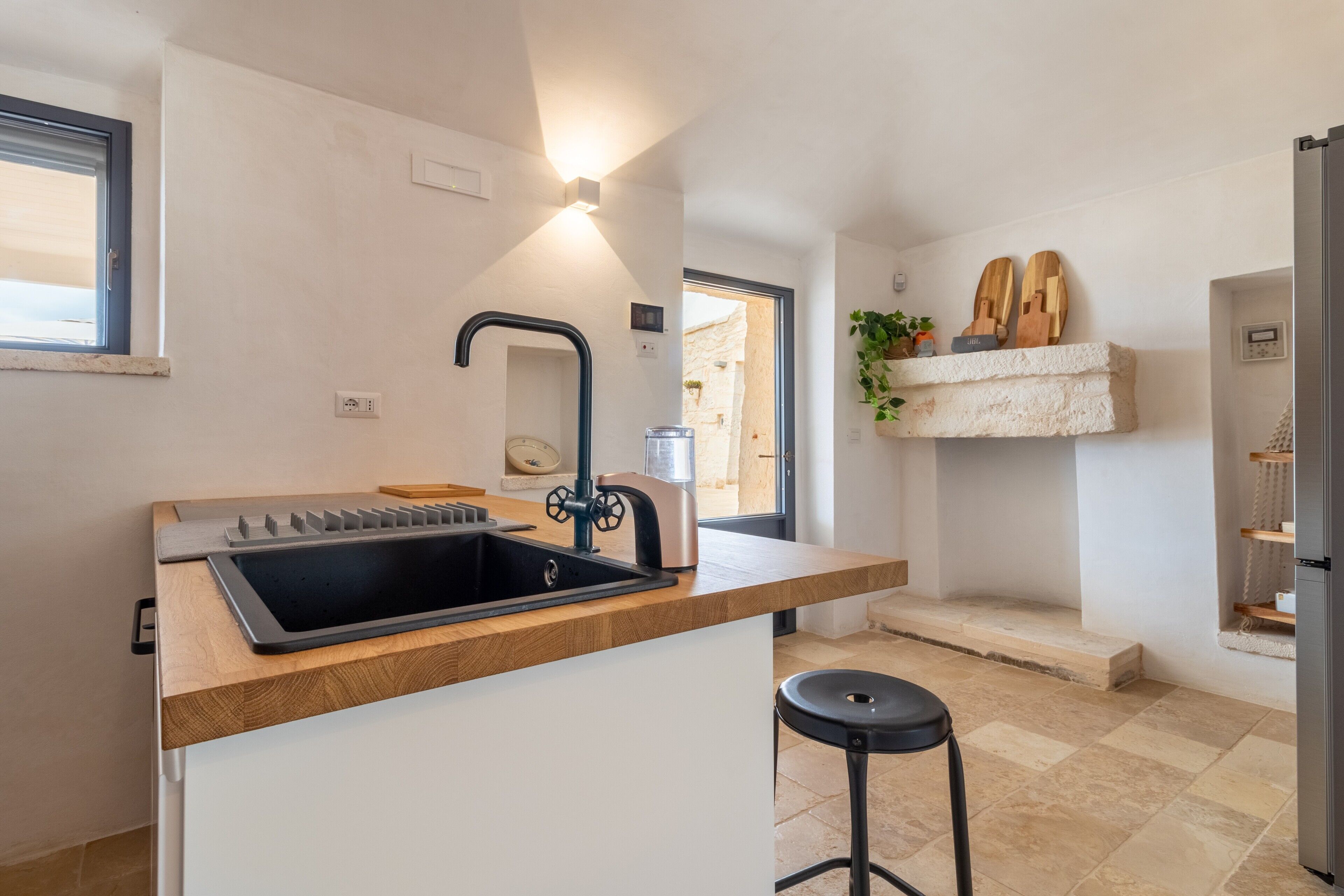 A kitchen with a black sink, wooden countertop, and a black stool.