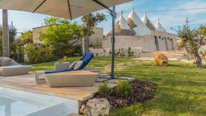 A poolside area with lounge chairs, a pergola, and a stone building with conical roofs. - Holiday Home 'Trulli Terralunga' with Pool and Wi-Fi (Martina Franca)