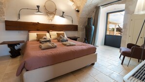 A bedroom with a large bed, a wooden headboard, a bedside table, a lamp, and a view of the outside. - Holiday Home 'Trulli Terralunga' with Pool and Wi-Fi (Martina Franca)