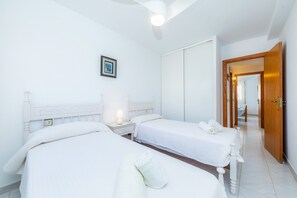 A hotel room with two beds, a bedside table with a lamp, a framed picture on the wall, and a wooden door. - Veleta Apartment with Sea Views, Shared Pool, Terrace, and Wi-Fi (Port pollença)