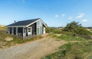 Una casa costera con entrada de grava, cerco de madera y vista a la playa.